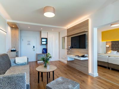 Camera d'hotel moderna con zona soggiorno, TV e vista sulla camera da letto.