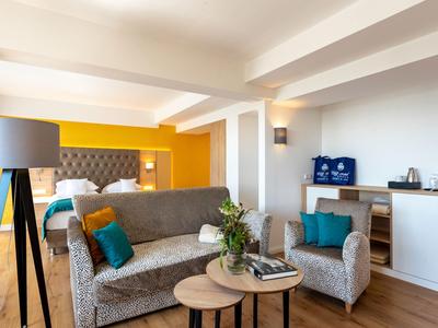 Camera d'hotel moderna con divano, poltrona, letto matrimoniale e scrivania.