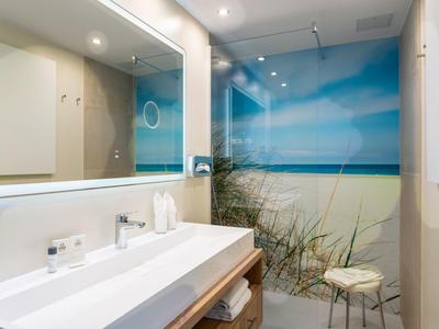 Bagno moderno con grande specchio e parete doccia a tema spiaggia.