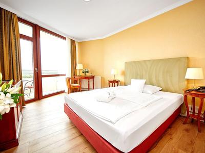 Camera d'hotel luminosa con balcone, letto matrimoniale e comodini con lampade.