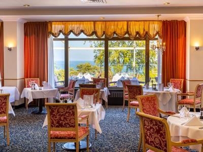 Ristorante elegante con tavoli davanti a grandi finestre con vista sul mare e sugli alberi.