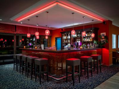 Bar dell'hotel moderna con illuminazione rossa, sgabelli e ampia selezione di bevande.