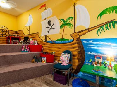 Sala giochi colorata per bambini con murale di nave pirata e giocattoli su gradini e tavoli.