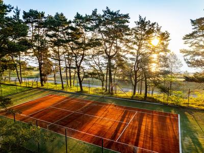 Campo da tennis in terra battuta all'alba, circondato da alberi e natura.
