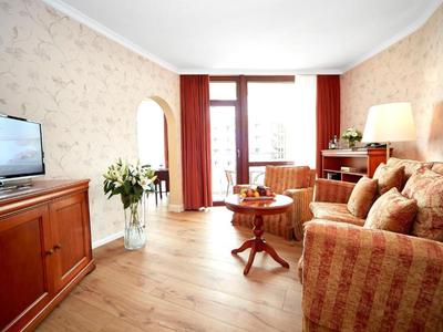 Soggiorno luminoso con divano, camino, TV e porta balcone con tende.