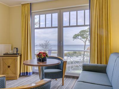 Camera d'hotel accogliente con divano, tavolo, sedia e vista mare attraverso grandi finestre