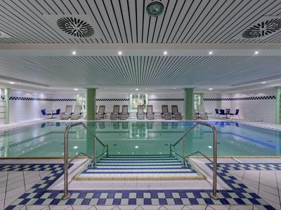 Indoor pool with green columns, water slide, loungers, and modern ceiling with ventilation