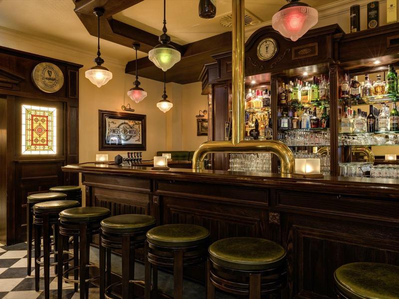 Cozy hotel bar with wooden furniture, dark stools, and decorative ceiling lamps.