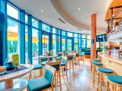 Bar de hotel luminoso con mostrador curvado, taburetes azules y ventanas panorámicas con vista al exterior.