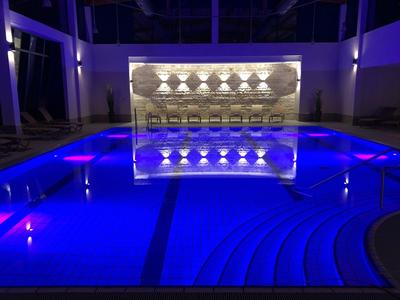 Osvětlený hotelový bazén s modrou vodou a moderním uměleckým dílem v pozadí v noci.