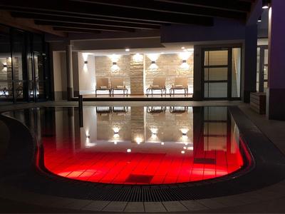 Foto nocturna de una piscina con iluminación roja y zona de asientos en un interior moderno.