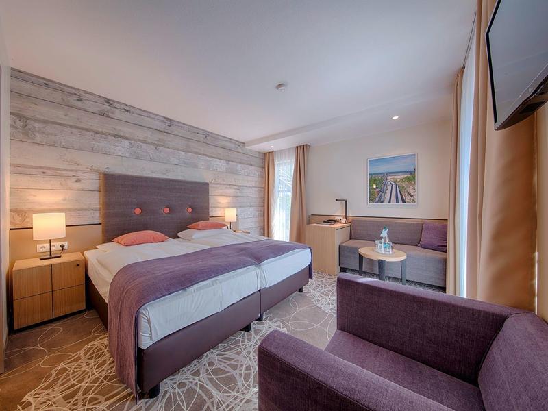 Pohodlný hotelový pokoj s manželskou postelí, posezením a moderním dekorem.