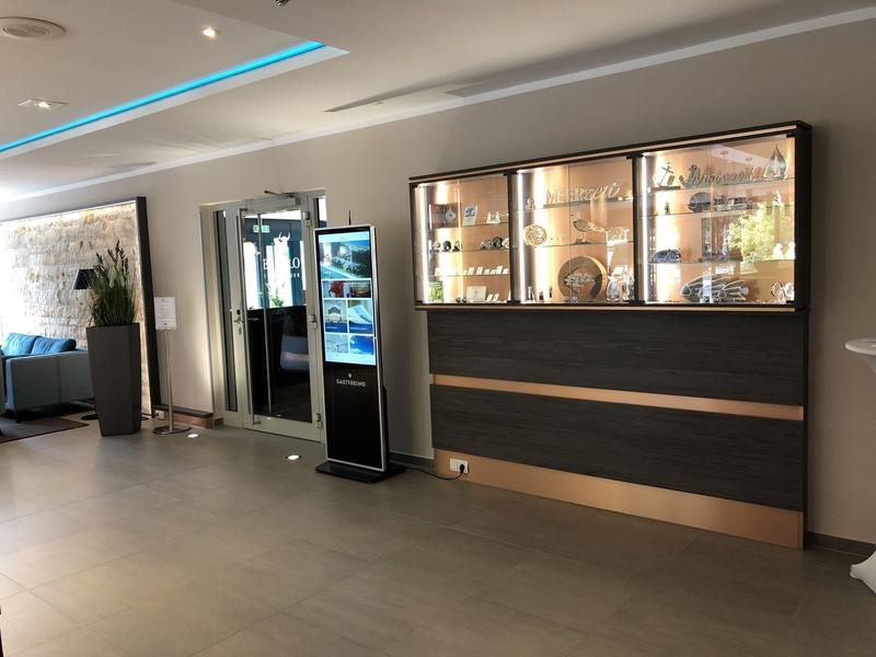 Moderní hotelová zóna s nápojovými automaty a osvětlenou skříní na šedé zdi.