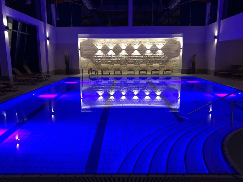 Osvětlený hotelový bazén s modrou vodou a moderním uměleckým dílem v pozadí v noci.