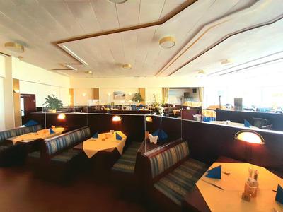 Wnętrze restauracji z ławkami, stołami i miękkimi siedziskami w ciepłym świetle.