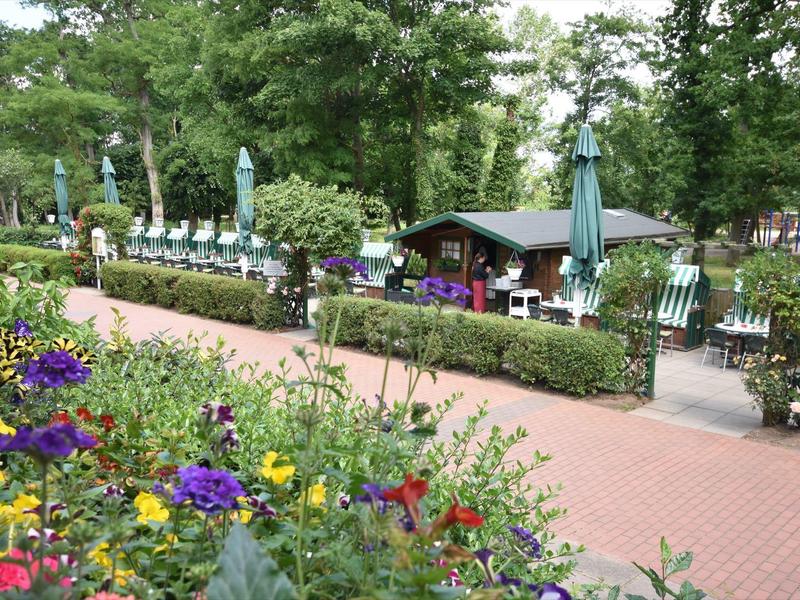 Bunter Blumengarten neben einem gepflasterten Weg und mehreren Sitzbereichen mit grünen Stühlen.