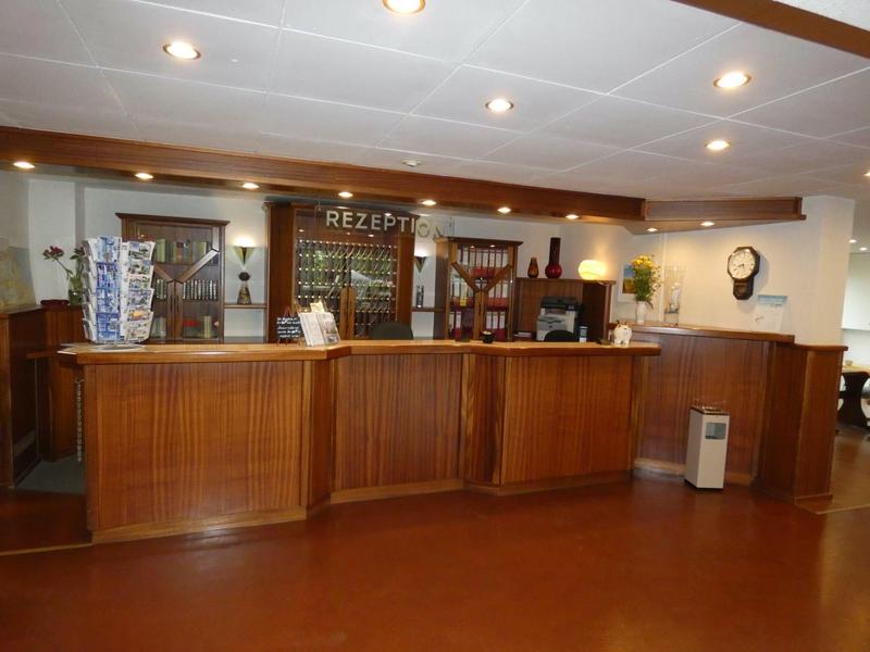 Rezeptionsbereich mit hölzernem Empfangstresen, Bücherregal, Uhr und Deckenbeleuchtung.