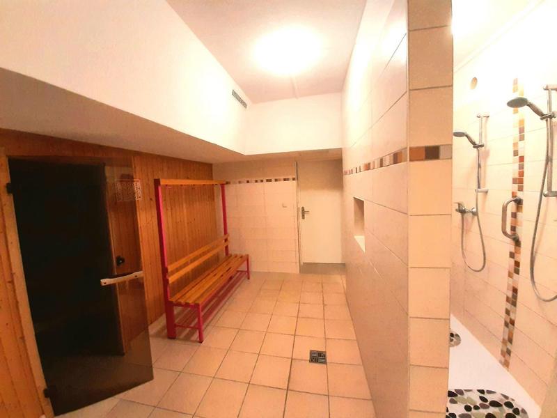 Hell beleuchteter Duschraum mit weißen Wandfliesen, mehreren Duschköpfen und roter Bank.