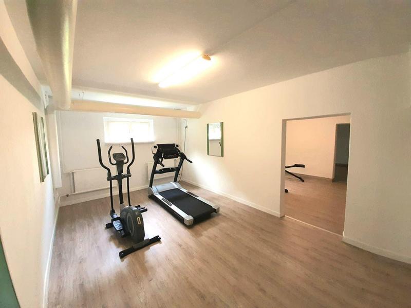 Heller Raum mit Holzboden, Crosstrainer und Laufband, offener Durchgang zu weiterem Zimmer.