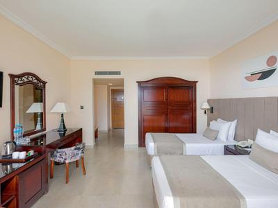 Helles Hotelzimmer mit zwei Betten, Holzmöbeln und Flachbildfernseher an der Wand.