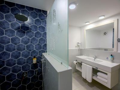 Modernes Hotelbad mit blauen sechseckigen Fliesen in der Dusche und weißem Waschbecken.