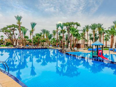 Großer Hotelpool mit Wasserrutsche, umgeben von Palmen und blauer Himmel.