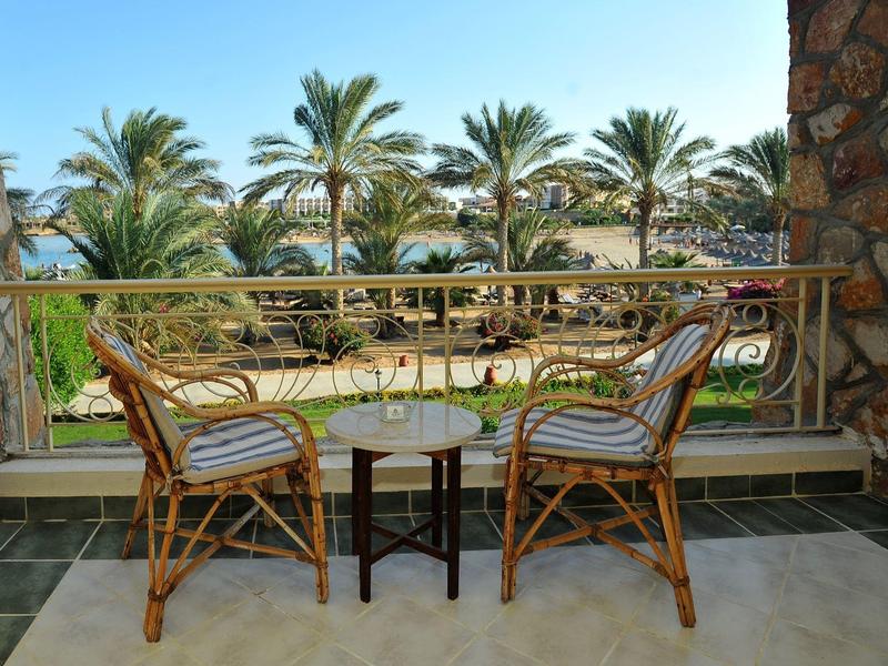 Balcony with two wicker chairs and a small table overlooking palm trees and ocean.