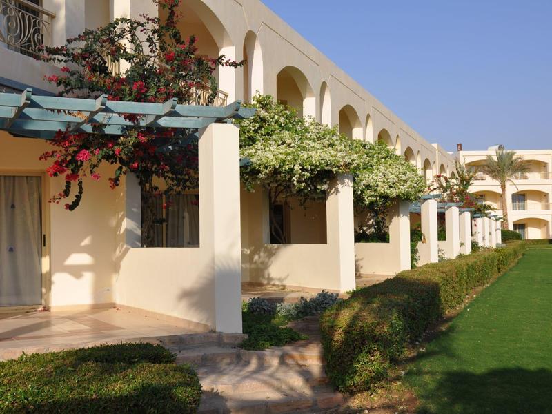Hotel building with balconies, greenery, and clear blue sky on a sunny day.