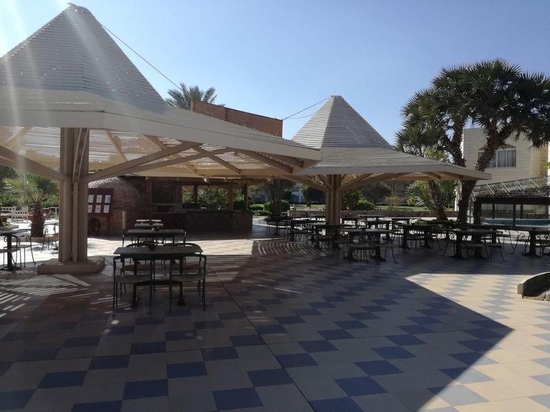 Outdoor seating area with tables and chairs under large umbrellas in a sunny hotel courtyard.