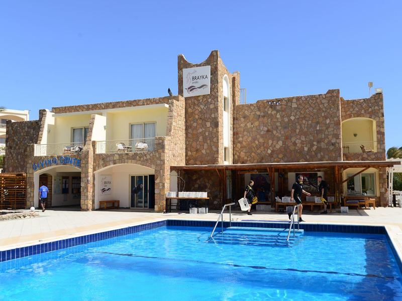 Hotel building with stone facade and outdoor swimming pool under clear blue sky.