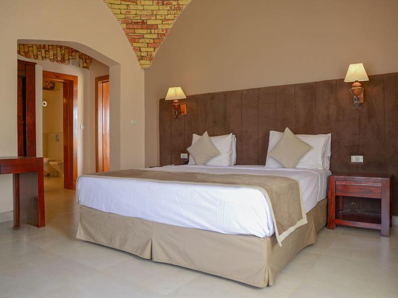 Modern hotel room with a double bed, nightstands, lamps, and arched doorway.