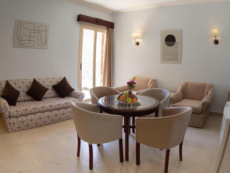 Bright living room with a sofa, four chairs around a round table, and two armchairs near a window.