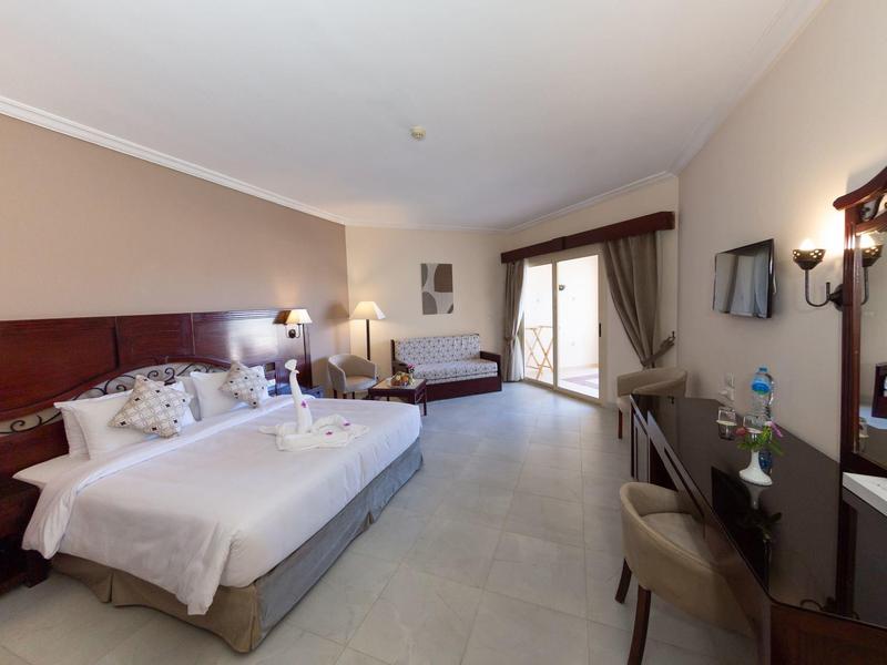 Spacious hotel room with double and single beds, desk, TV, and balcony door.
