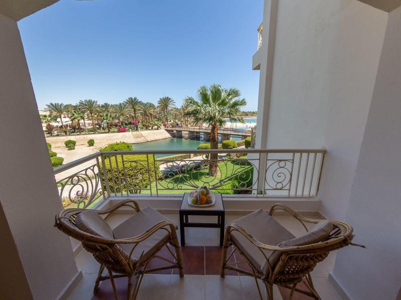 Balcony with two wicker chairs and table overlooking palm trees and pool area.
