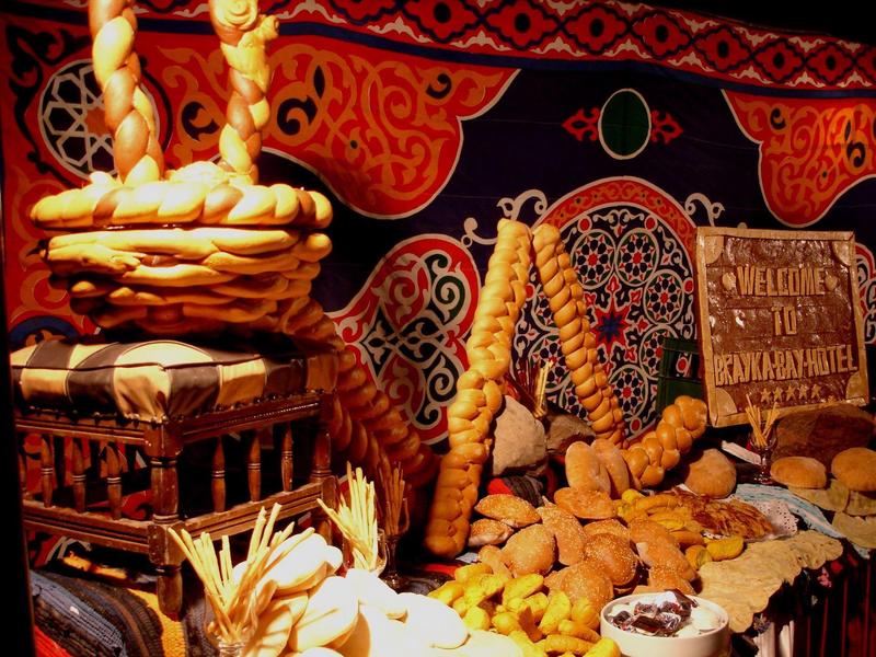 Display of traditional pastries and breads with a welcoming sign on a decorative cloth background.