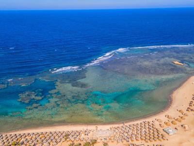 Strand mit blauem Wasser und Reihen von Sonnenschirmen und Liegestühlen am Sandstrand
