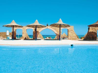 Blauer Pool mit Strohdach-Sonnenschirmen, Liegestühlen und einem blauen Himmel im Hintergrund.