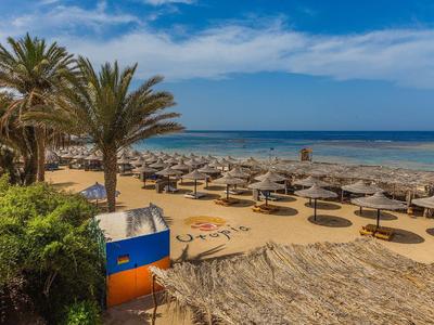 Beach with palm trees, sun loungers, and umbrellas by the sea on a clear day.