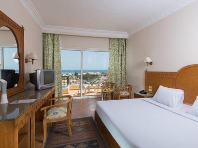 Bright hotel room with double bed and city view through large windows.