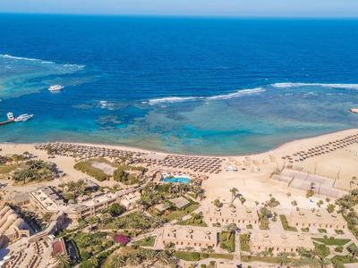 Aerial view of a beach resort with sun loungers, pools, and clear blue sea.