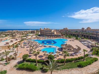 Große Hotelanlage mit mehreren Pools und Palmen unter klarem blauem Himmel am Meer.