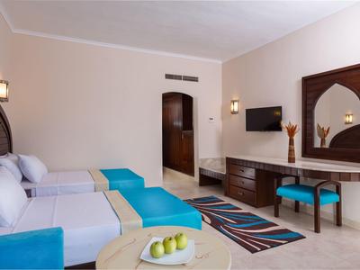 Hotelzimmer mit zwei Einzelbetten, blauem Sitzbereich und Spiegel über einem Schreibtisch.