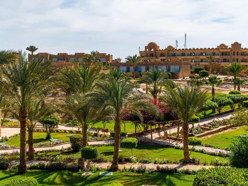 Luxury hotel with palm trees and manicured garden under a partly cloudy sky.