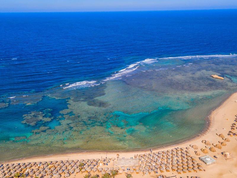 Aerial view of a beach with sun umbrellas and clear turquoise water by the sea.