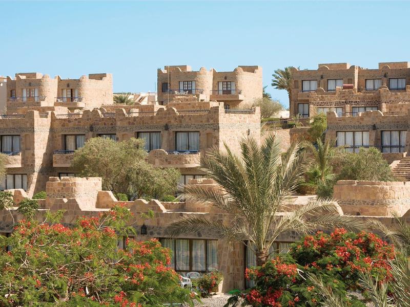 Sandstone-colored hotel buildings with flat roofs and lush vegetation in the foreground