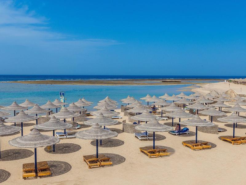Beach with many straw sunshades and calm blue sea in the background.