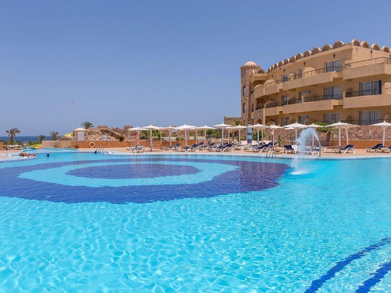 Large outdoor pool in front of a hotel with clear blue sky in the background.