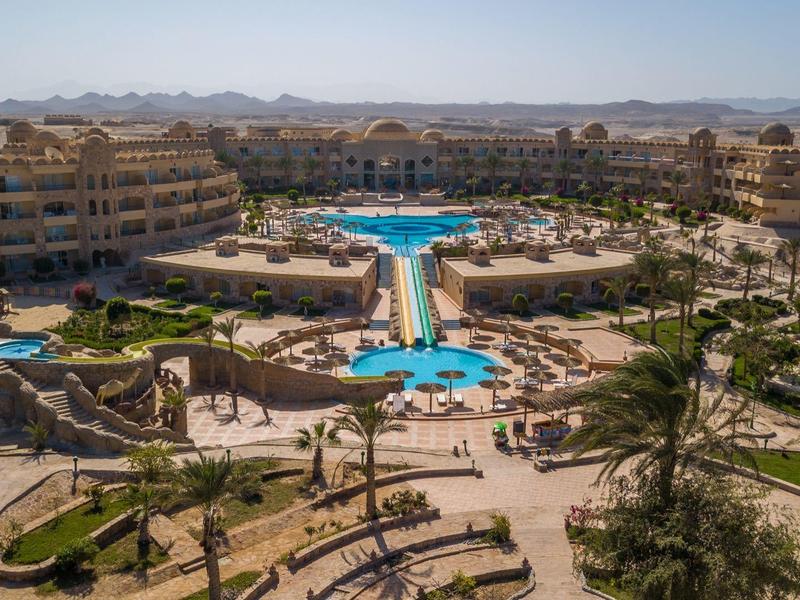 Large hotel complex with multiple pools and sun loungers in a desert landscape.
