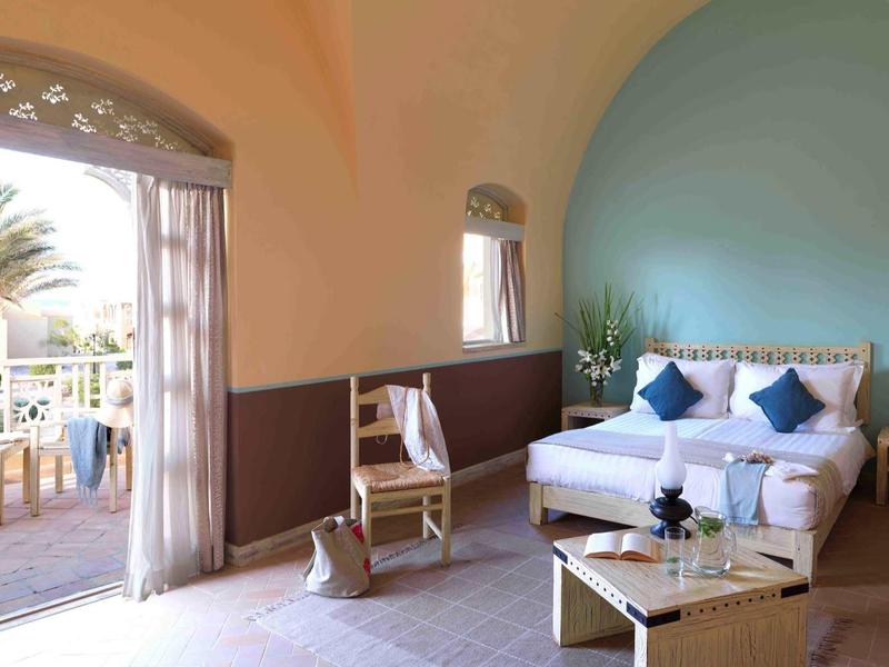 Bright room with double bed, blue cushions, armchair, and balcony access with sea view.