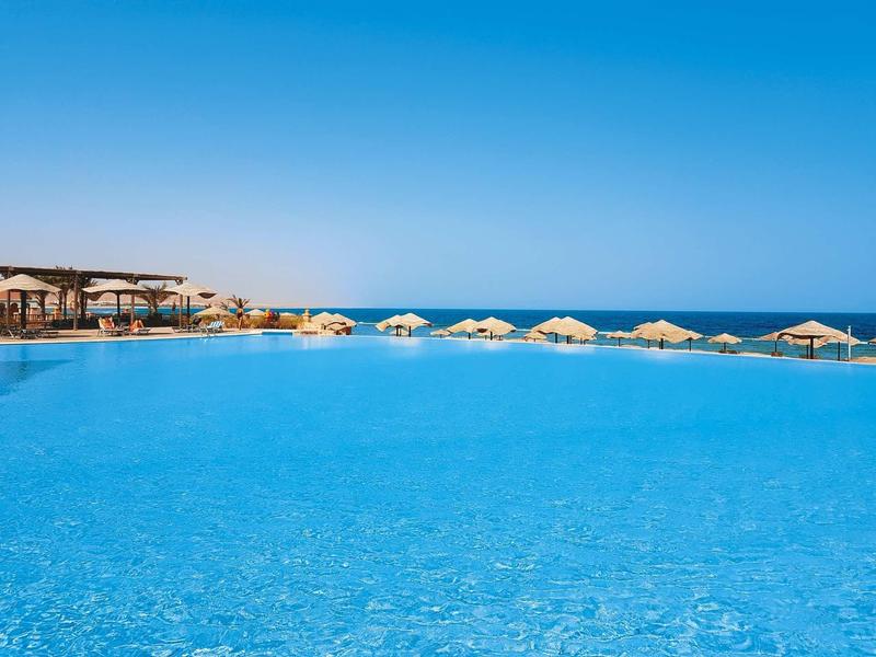 Large pool with sun umbrellas and sea view under clear blue sky.